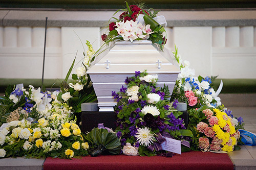 En kista med blomsterhyllningar, framme vid altaret i kyrkan.