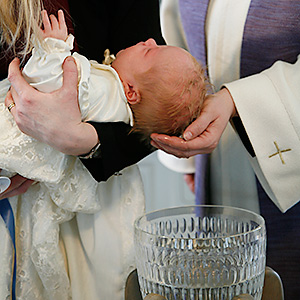 Ett barn som hålls ovanför dopfunten där prästen öser vatten över huvudet