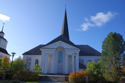Pedersöre kyrka sedd från huvudingången. Träd och buskar i höstskrud.