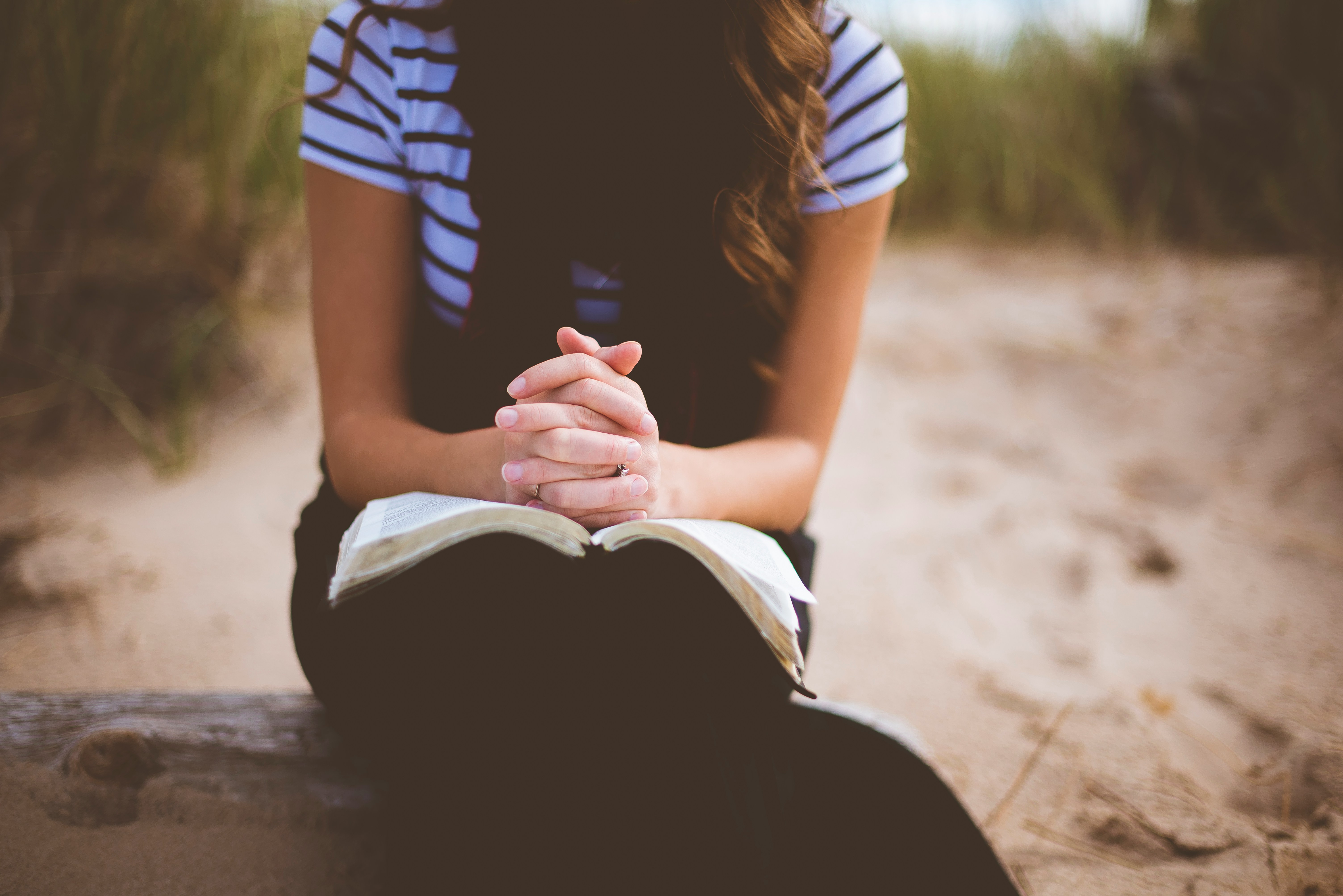 Kvinna med knäppta händer på en öppen bibel. Ansiktet syns inte.