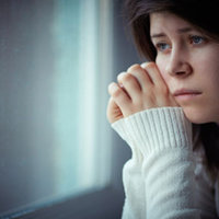 En ung kvinna tittar ut genom fönster med sorgsen min